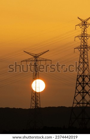 Sun disk at sunset. silhouette of high voltage line poles in orange sunset colors. Istanbul's energy transmission lines. Vertical photo. No people, nobody. Natural and traditional energy sources.