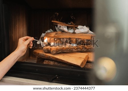 Female hand holds a matchstick, ready to ignite the firewood in a fireplace. Royalty-Free Stock Photo #2374444377