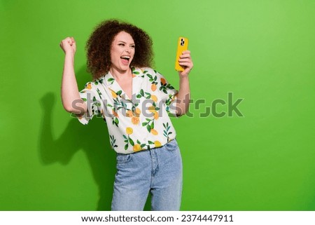 Photo of charming lucky girl dressed print shirt rising fist winning game modern gadget empty space isolated green color background