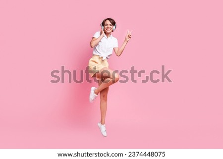 Full length body photo of showing v sign cheery smiling youngster girl enjoying her new headphones in air isolated on pink color background