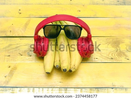 Creative ripe bananas in musical headphones and sunglasses. Bananas listening to music on a wooden yellow background. Ripe vitamin fruit banana