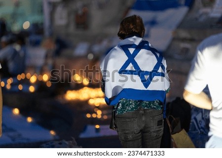 Lisbon, Portugal October 10, 2023. A woman at the memorial to the fallen Israelis in October 2023 at dusk, , with the flag of Israel on her shoulders Royalty-Free Stock Photo #2374471333