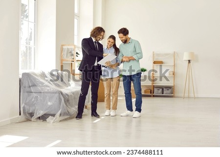 Young family buying new property. Happy married couple together with real estate agent sign contract in fully furnished white spacious Scandinavian living room interior in modern house or apartment Royalty-Free Stock Photo #2374488111