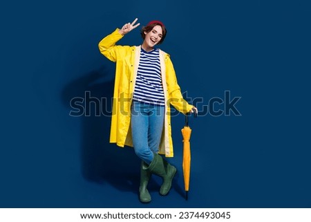 Full length body photo of funky girlfriend walking in park showing v sign bring umbrella waiting rain isolated on blue color background
