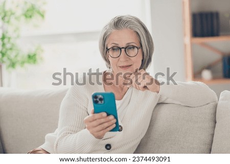 Photo of thoughtful clever senior lady dressed white cardigan eyewear reading apple samsung iphone modern device indoors house room