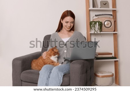Happy woman with cat working in armchair at home Royalty-Free Stock Photo #2374509295