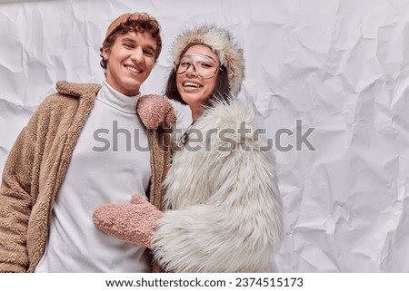 joyful interracial couple in fashionable warm outwear on white textured backdrop, winter fashion Royalty-Free Stock Photo #2374515173