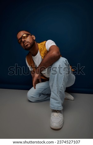 african american man with beard and sunglasses sitting on floor looking at camera, fashion concept