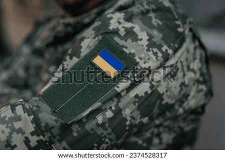 Ukrainian soldier in military uniform with the national flag on his shoulder. Dramatic background, cold colors. Concept of war and peace, conflict between Ukraine and Russia.