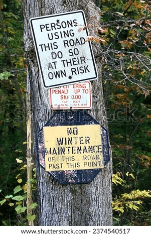 Warning signs on tree trunk. Use at own risk. No winter maintenance. No littering. Fines. Posted sign. Close up. Information. Weathered. Grungy. Grunge. Rustic. Rural Country. Countryside. Fall autumn