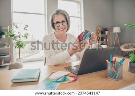Photo of positive charming senior lady dressed white cardigan holding colors indoors house room