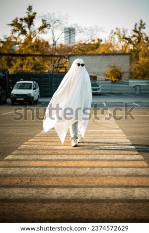 Celebrating halloween. Ghost Challenge 2021. A man dressed as a ghost from a sheet and sunglasses crosses the road along the crosswalk. Spooky season.