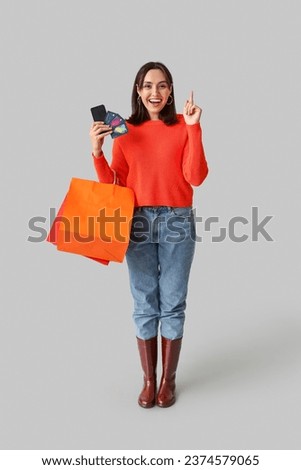 Young woman with shopping bags, credit cards and mobile phone pointing at something on grey background