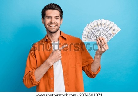 Photo of pretty positive guy wear orange shirt pointing finger money fan isolated blue color background