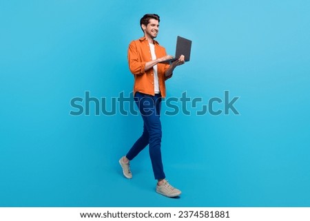 Full body profile photo of attractive cheerful young person hold use netbook walking isolated on blue color background