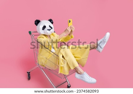 Full body photo of weird 3d panda mask lady sit inside store pushcart hold smart phone make selfie isolated on pink color background