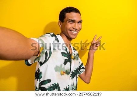 Portrait of positive cheerful guy wear print clothes with ring in nose show v-sign making selfie isolated on yellow color background
