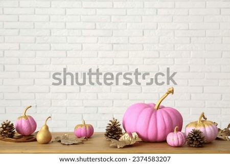 Pink painted pumpkins with autumn leaves and cones on wooden table near white brick wall