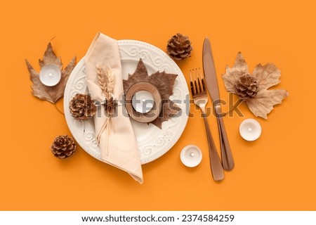 Autumn table setting with dried leaves, cones and burning candles on orange background