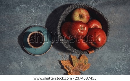 Red juicy apples in a gray woven basket on a gray background. coffee cup near by basket