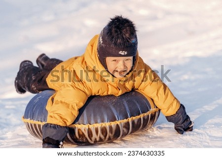 Active toddler boy in a yellow jacket sliding down the hill on snow tube.Winter fun,active lifestyle concept. Royalty-Free Stock Photo #2374630335