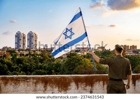A guy in a soldier's uniform with an Israeli flag in his hand against a cloudy sky. Remembrance Day - Yom HaZikaron, Patriotic holiday, Israeli Independence Day - Yom Ha'atzmaut concept. Royalty-Free Stock Photo #2374631543