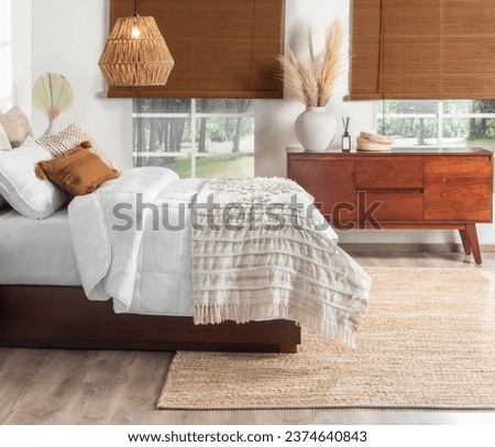 Welcoming Bedroom: King-Sized Bed Dressed in Soft White Quilts with Delicate Stitch Detailing, Accented by Cozy Textured Pillows in Earthy Tones, Rich Mahogany Bedside Wooden Cabinet, Area Rug. Royalty-Free Stock Photo #2374640843