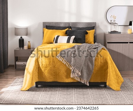Vibrant Bedroom Atmosphere, Quilted Yellow Comforter Contrasting with Monochrome Throw Blanket on Cozy bed, Accented by Sleek Gray Nightstand, Minimalist Wooden Dresser, Over a Complementary Area Rug. Royalty-Free Stock Photo #2374642265