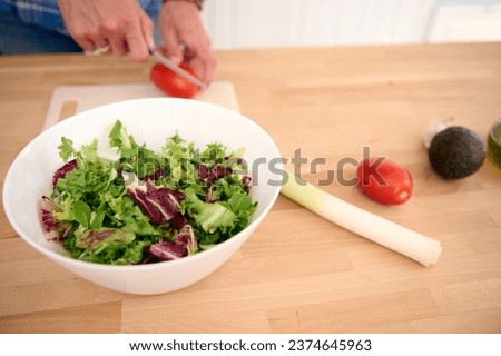 Close-up hands of a male chef chopping ripe organic tomatoes while preparing a delicious healthy salad from fresh vegetables and herbs. People. Food. Healthy eating, alimentation and dieting concept Royalty-Free Stock Photo #2374645963