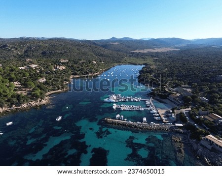 Picture of a beautiful port in Corsica in Propriano. In the background there are mountains, a village and turquoise water.