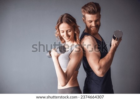 Beautiful young sports people are working out with dumbbells and smiling, on gray background