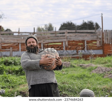 Bearded man holds pumpkin in his hands during autumn harvest in the garden