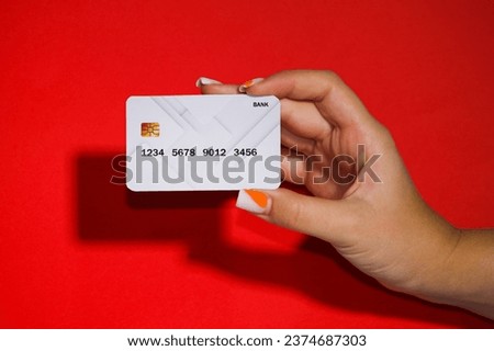 Picture on a red background with a woman's hand holding a white bank card, a very beautiful and rare color.