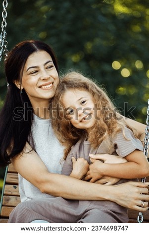 Happy summer time. Little daughter hugging her young happy mom in the park.