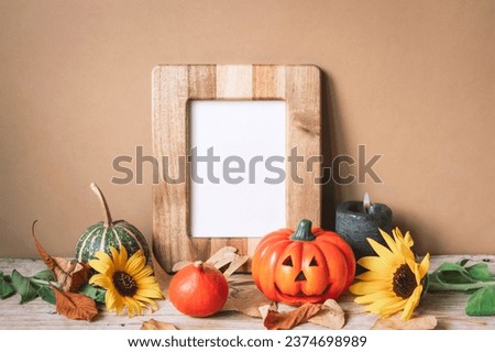 Blank picture frame and pumpkins, sunflowers and dry leaves against beige wall. Halloween concept, mockup.
