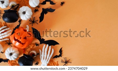 Close-up holiday decor: pumpkins, spiders, bats,pots, human skeleton hands, autumn leaves and eyes on an orange background,top view,copy space.Halloween celebration concept,decor for All Hallows' Day.