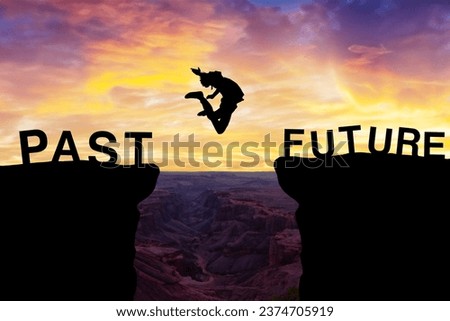 Silhouette of a person leaping between cliffs labeled 'PAST' and 'FUTURE'. Vibrant sunset illuminates a deep canyon below, symbolizing risk, growth, and change Royalty-Free Stock Photo #2374705919