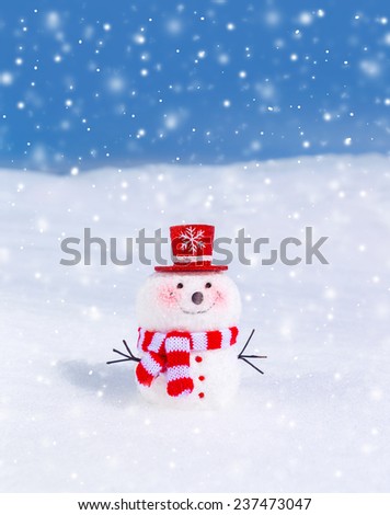 Cute snowman outdoors in snowy weather, traditional winter decoration, little smiling snowman wearing red hat and scarf, Christmas greeting card