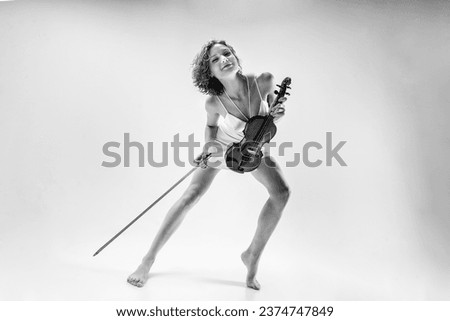 a young blonde female musician plays the violin moving on one leg