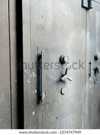 Big massive safe box made from strong metal material. Safe door handle and lock with spray paint stained surface isolated on vertical photography ratio. Industrial safety themed image.