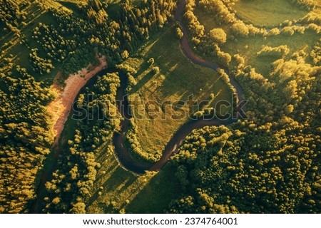 Small narrow winding river, green fields and forest aerial view. Green beautiful rural drone landscape in sunset light. Nature, sustainable and ecology concept. Top down view. Beautiful nature texture Royalty-Free Stock Photo #2374764001