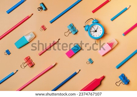 Creative student desk modern school supplies on neutral pastel beige background. Top view flat lay. Back to school concept. Diagonal pattern with pencils, pens, markers, alarm clock, stationery clips