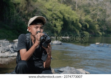 Asian cute boys holds binoculars and joining the birdwatching activity at the local national park, new edited, concept for nature and environment study of young people around the world.