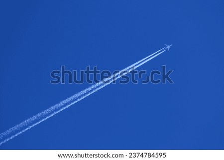 Airplane in the blue sky with white contrails Royalty-Free Stock Photo #2374784595