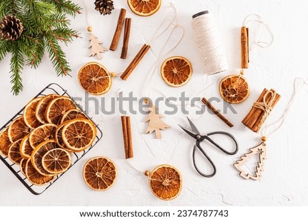 Top view of white textured background with homemade garland of dried oranges, spruce branches, orange slices and craft scissors. Flat lay. decoration Royalty-Free Stock Photo #2374787743