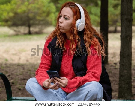 A girl with headphones in the park listens to music. A young girl rests in the park on a sunny day.