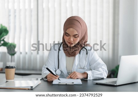 Young muslim female doctor in brown hijab headscarf working with medical papers while sitting in modern clinic office
