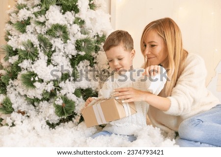 Smiling mom and happy son open gift bag under Christmas tree. Concept of holiday joy and giving presents. Happy family. New Year morning