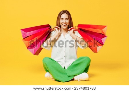 Full body young woman wear white casual clothes sit hold in hand paper package bags after shopping walking go isolated on plain light yellow color background studio. Black Friday sale buy day concept