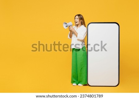 Full body sideways young caucasian happy woman she wears white shirt casual clothes big huge blank screen mobile cell phone smartphone with area scream in megaphone isolated on plain yellow background